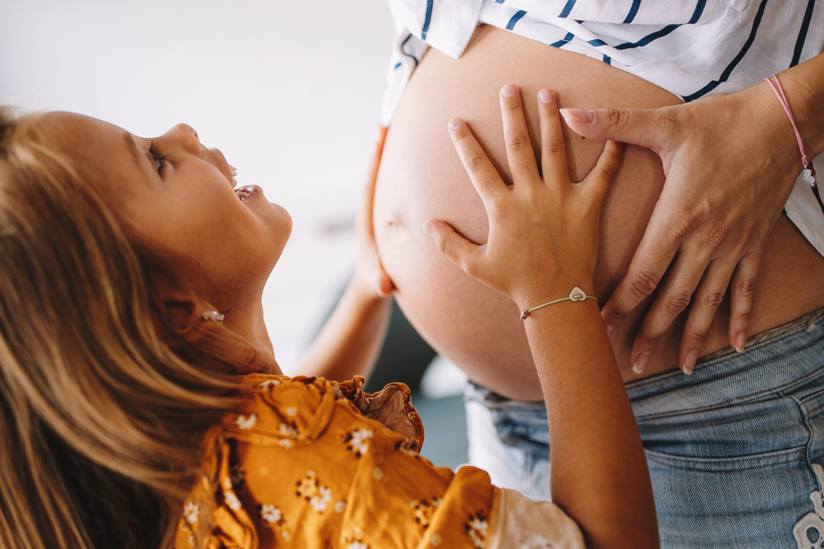 Schwangere Frau mit Tochter, die ihre Hände auf den Babybauch legt