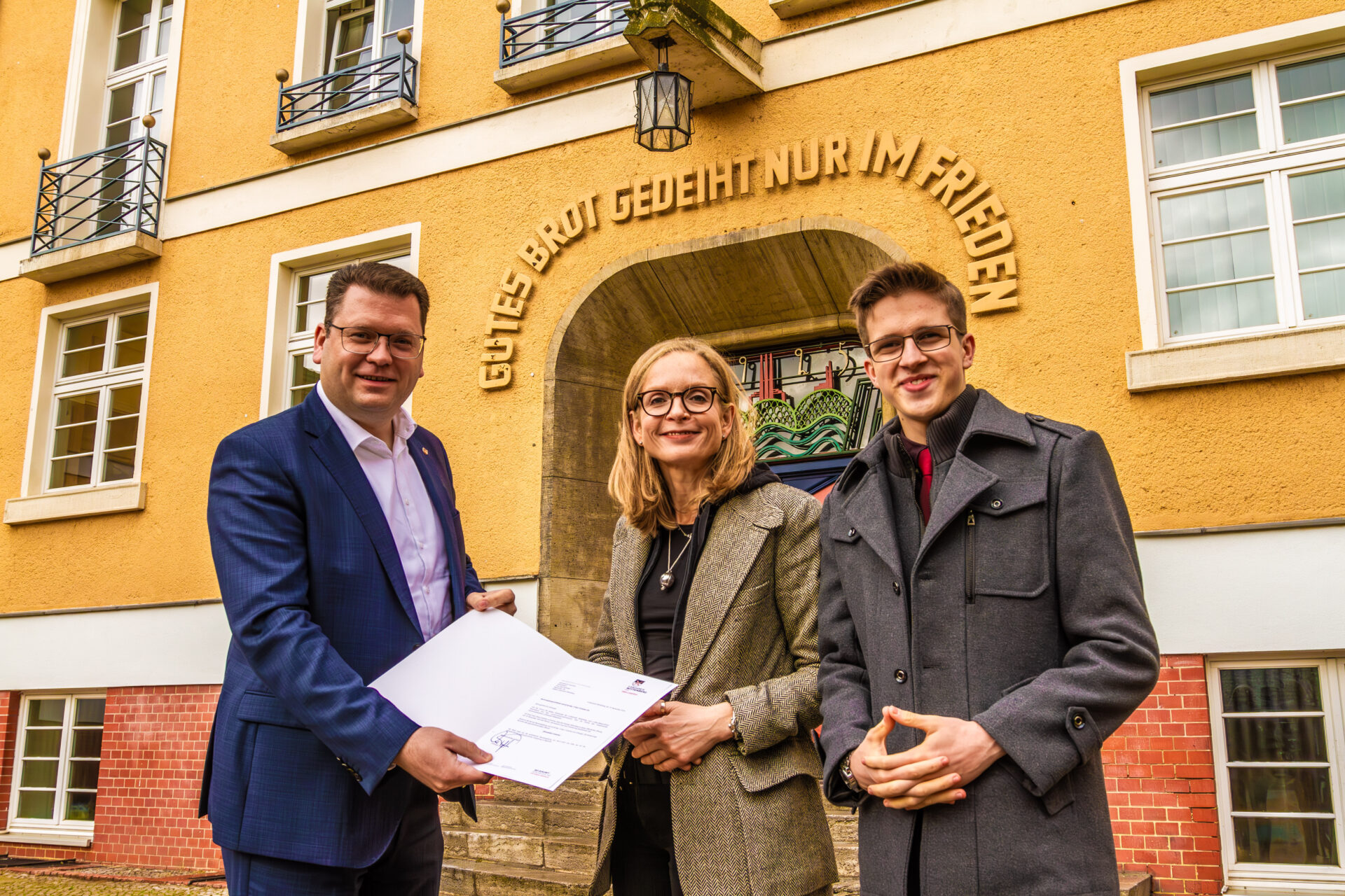 Landrat Christian Tylsch (links) übergibt Schulleiterin Anja Aichinger (Mitte) das offizielle Schreiben zur Umbenennung des Gymnasiums. Rechts im Bild: Schülersprecher Meldrick Stern.